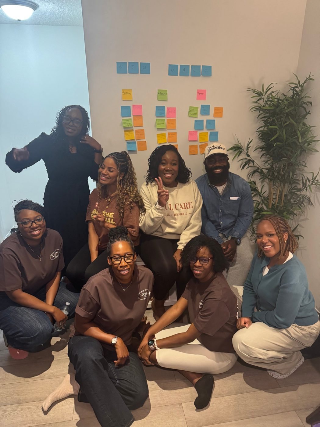 The Soul Care team gathered in front of a win wall of sticky notes during a team session